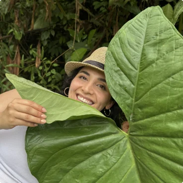 Gaby smiling behind a giant leaf in the rainforest